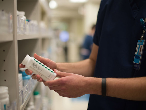 Male pharmacist holding and looking at a pill bottle in pharmacy