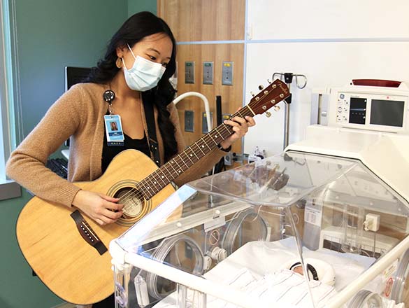 Music therapist playing guitar and singing to a NICU baby