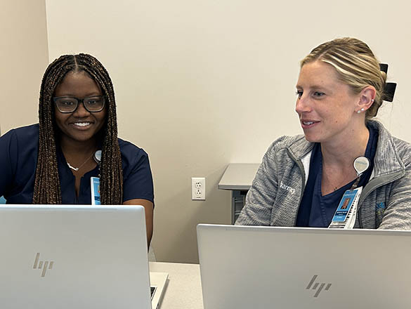 Two People Working Side by Side on Two Computers Smiling