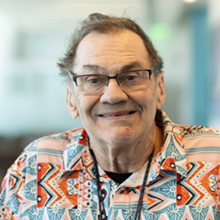 A smiling wearing glasses and a vibrant patterned shirt